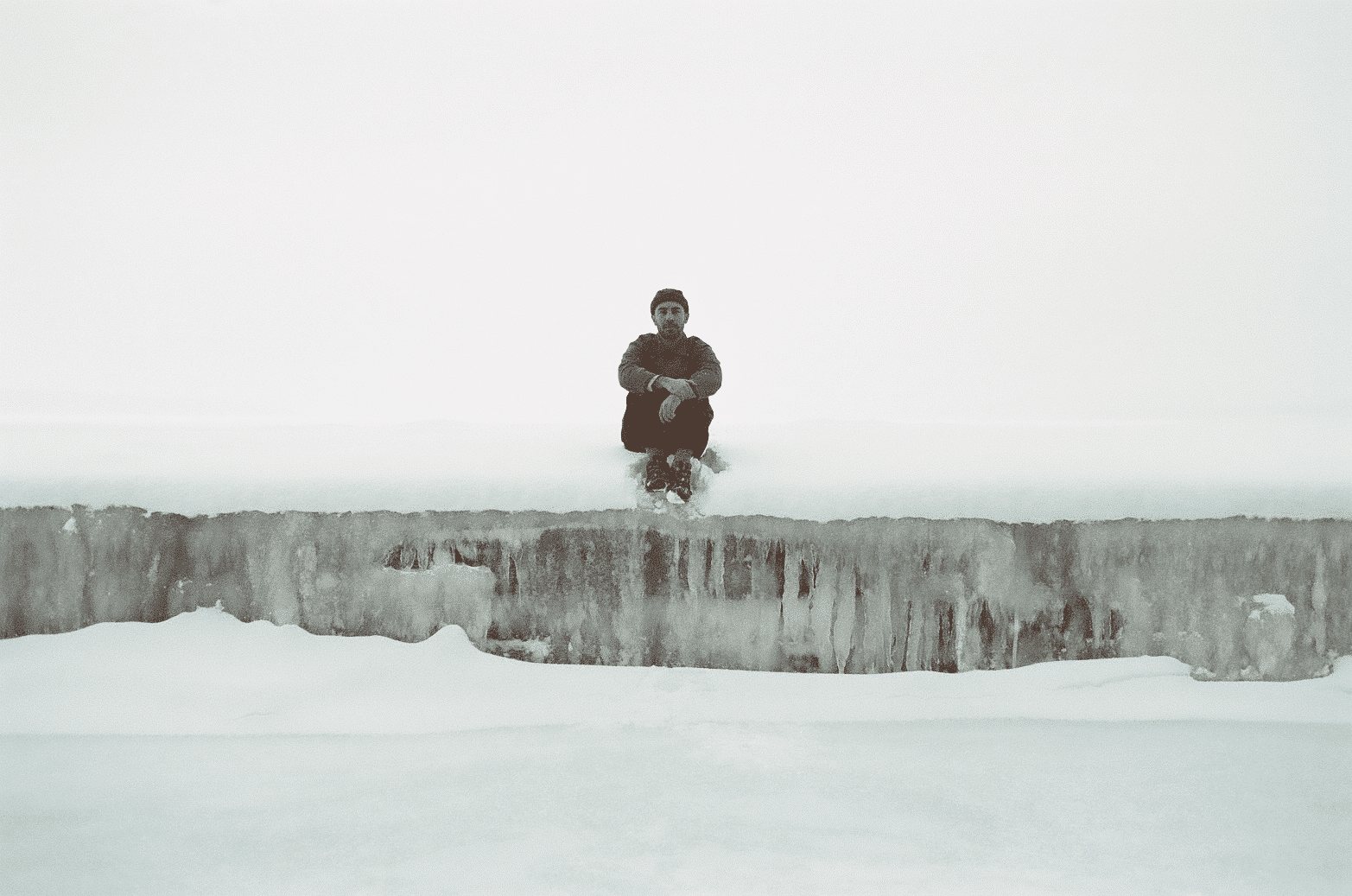 A photograph shows musician Peter Coccoma sitting in a frozen, snow-covered landscape. In the foreground of the picture is a cross-section of jagged ice that crosses the frame. Photo by Elori Saxl.