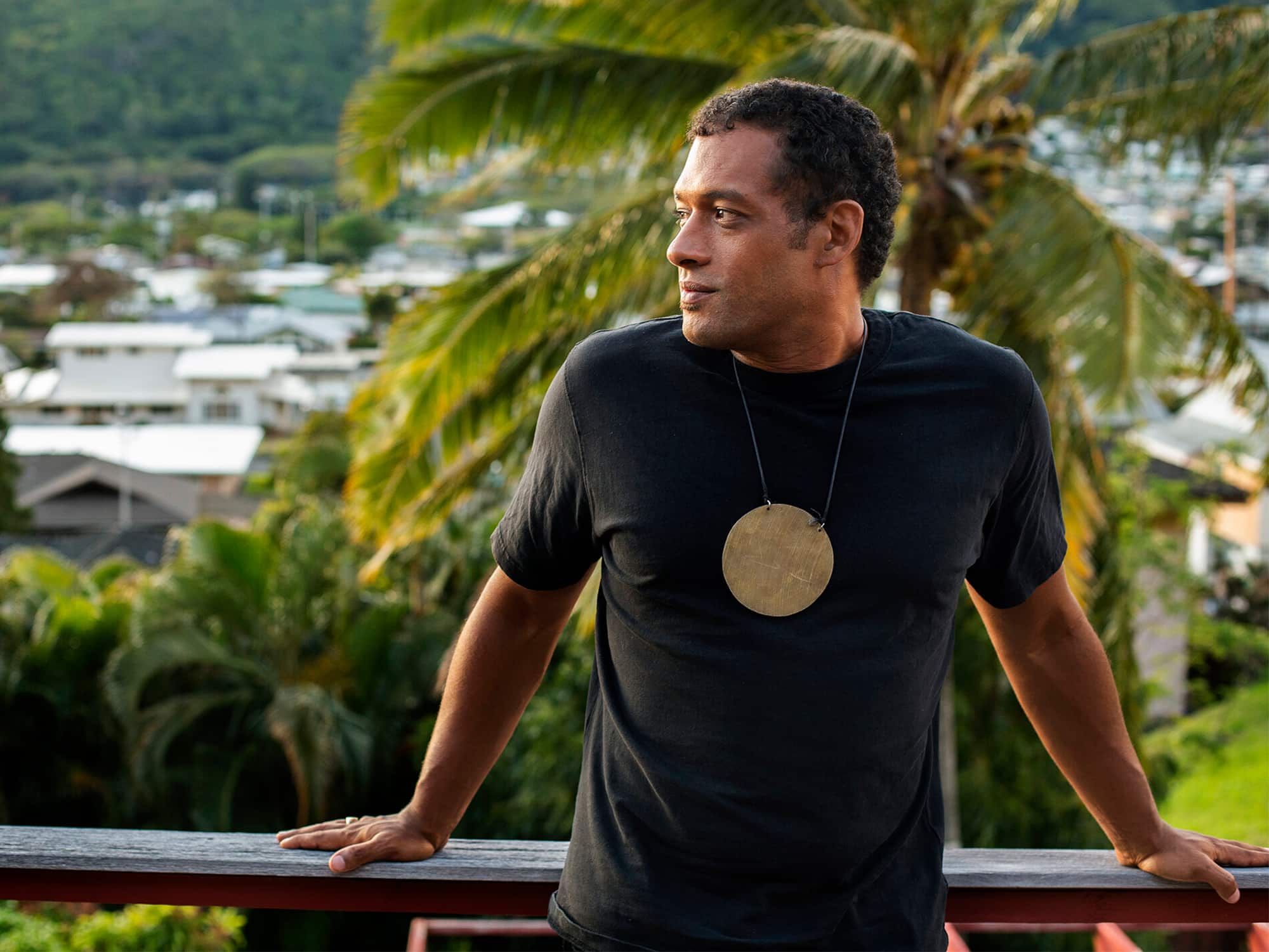 Makaya McCraven is shown standing outdoors, against a background of palm trees and the roofs of houses. Photo by Michael McDermott.