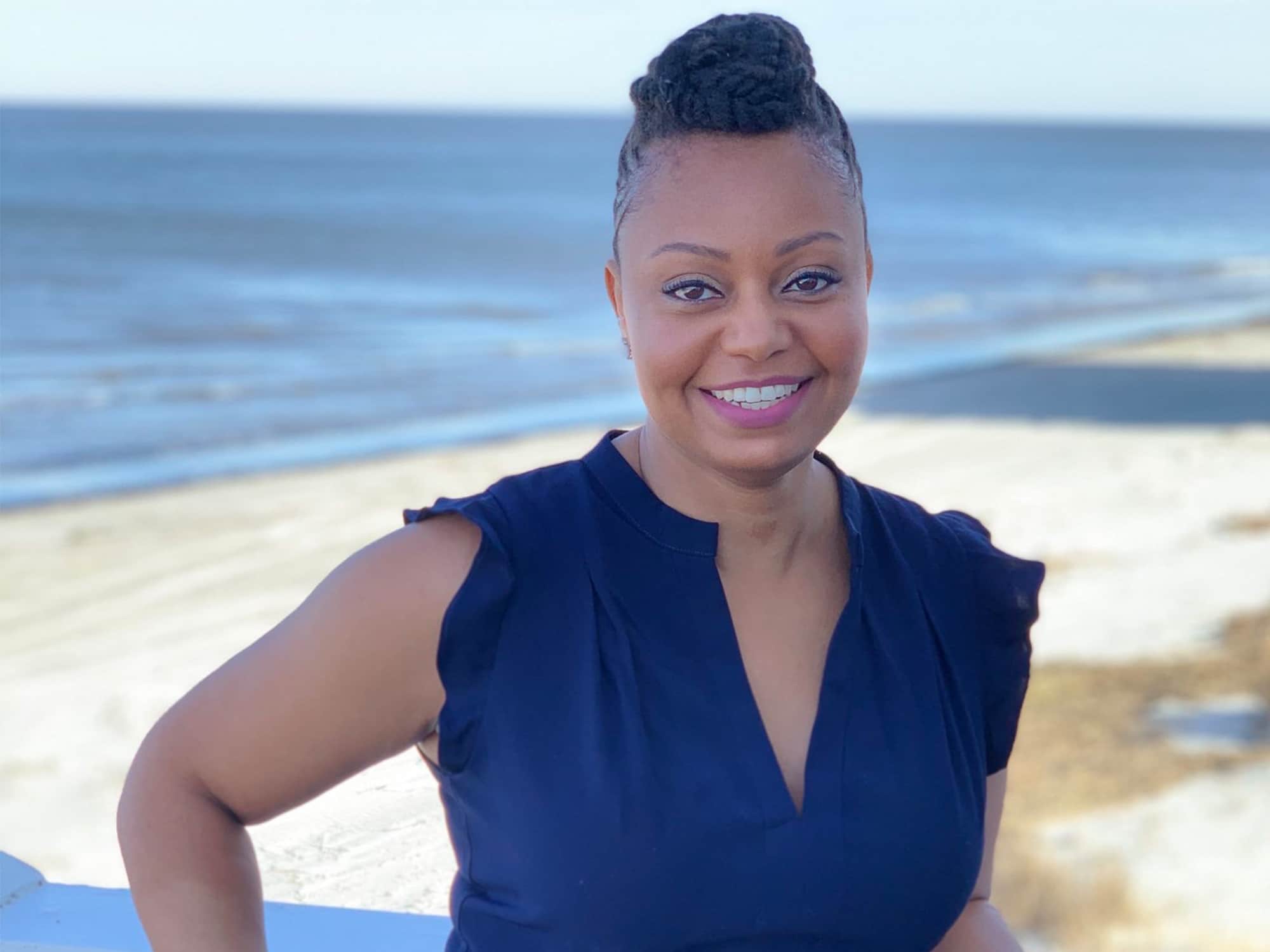 Jessica Williams is shown in a posed photo, smiling at the camera. Behind Williams is a sunny beach. Photo courtesy of Freedom Inc.