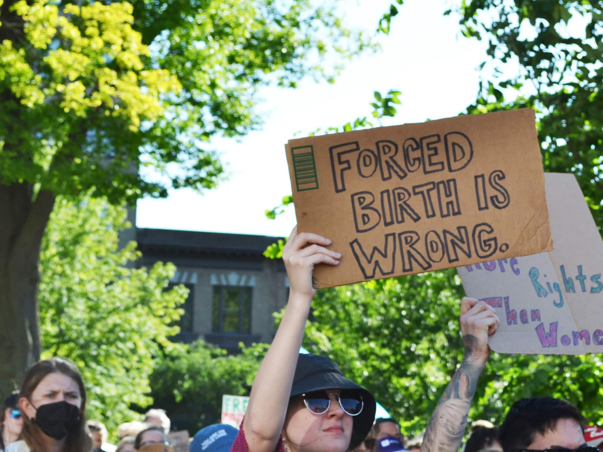 A protestor at a June 24, 2022 demonstration in downtown Madison holds up a handmade cardboard sign reading "FORCED BIRTH IS WRONG."