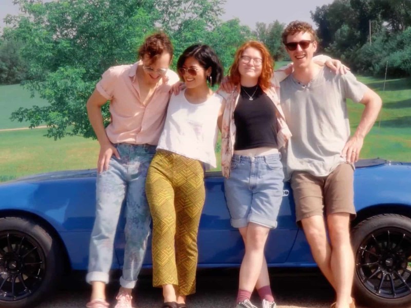 The four members of LINE are shown leaning against a blue convertible.