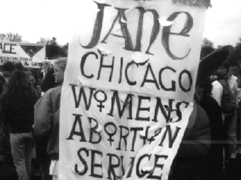 A member of the Jane Collective carries the group’s banner at a protest in Chicago. The women's gender symbol ♀ substitutes for the all the letter Os in "Women's Abortion" Service.