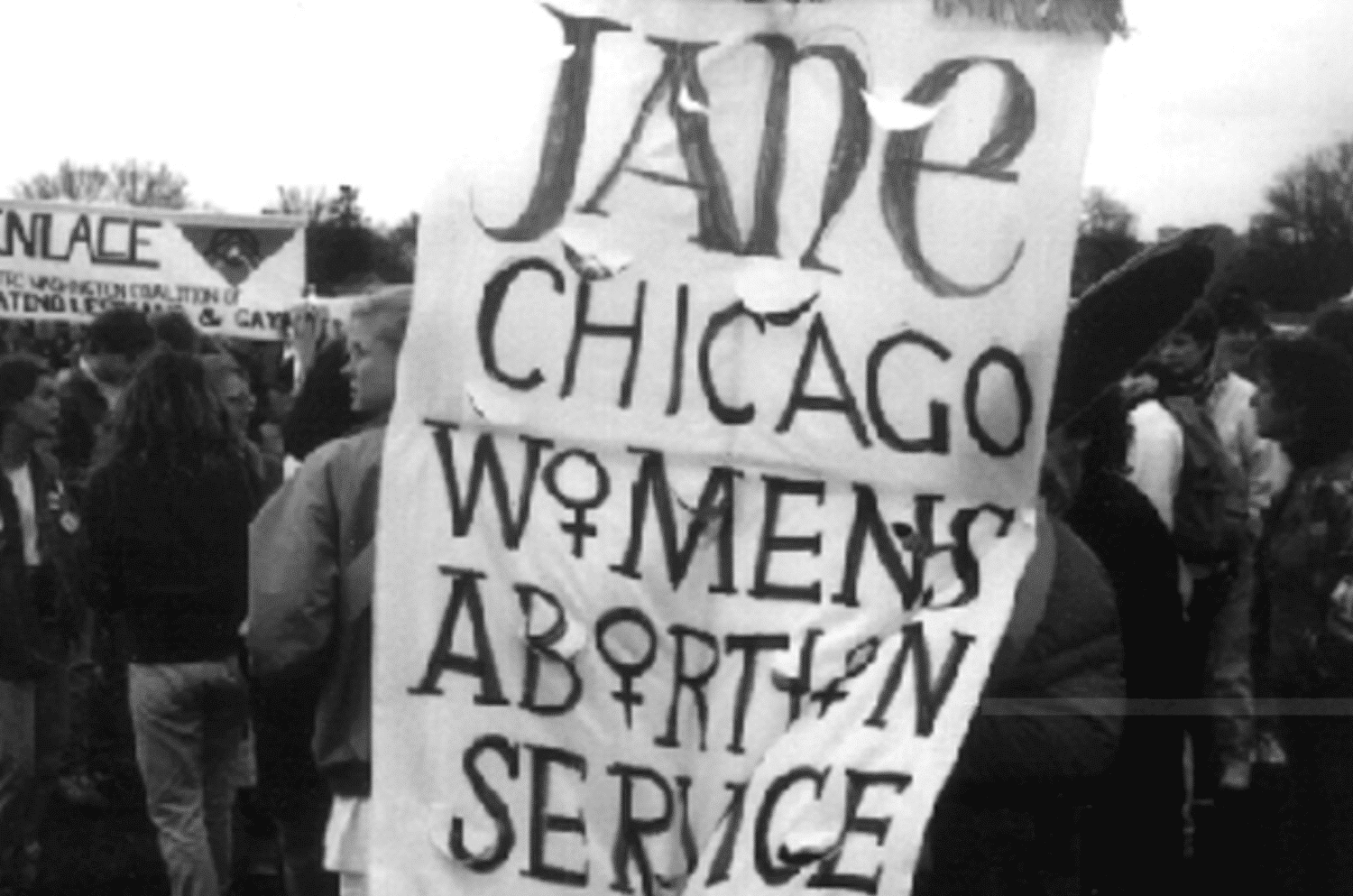 A member of the Jane Collective carries the group’s banner at a protest in Chicago. The women's gender symbol ♀ substitutes for the all the letter Os in "Women's Abortion" Service.