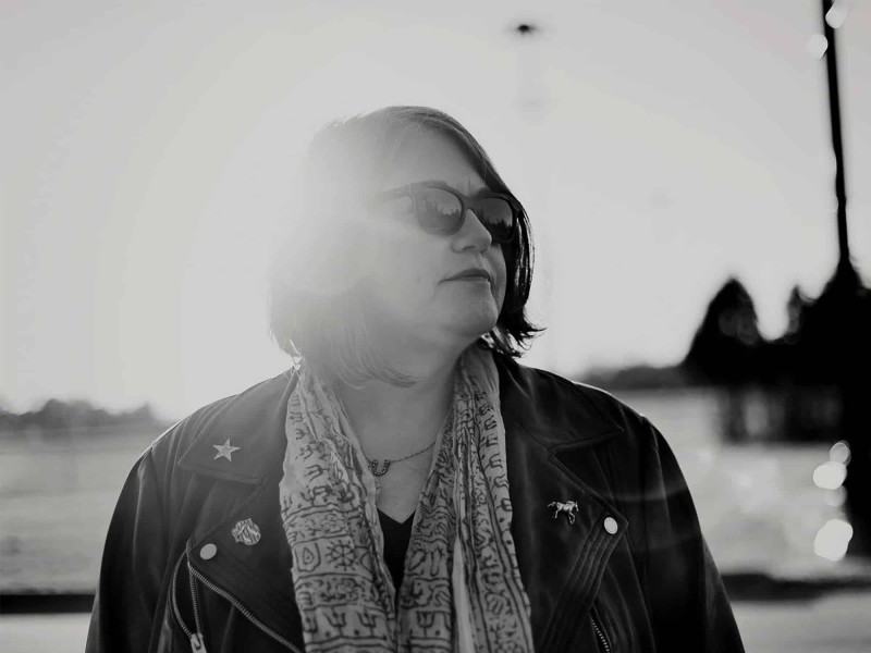 A black-and-white photo shows author Caryn Rose posing outdoors, looking off toward the side of the frame.