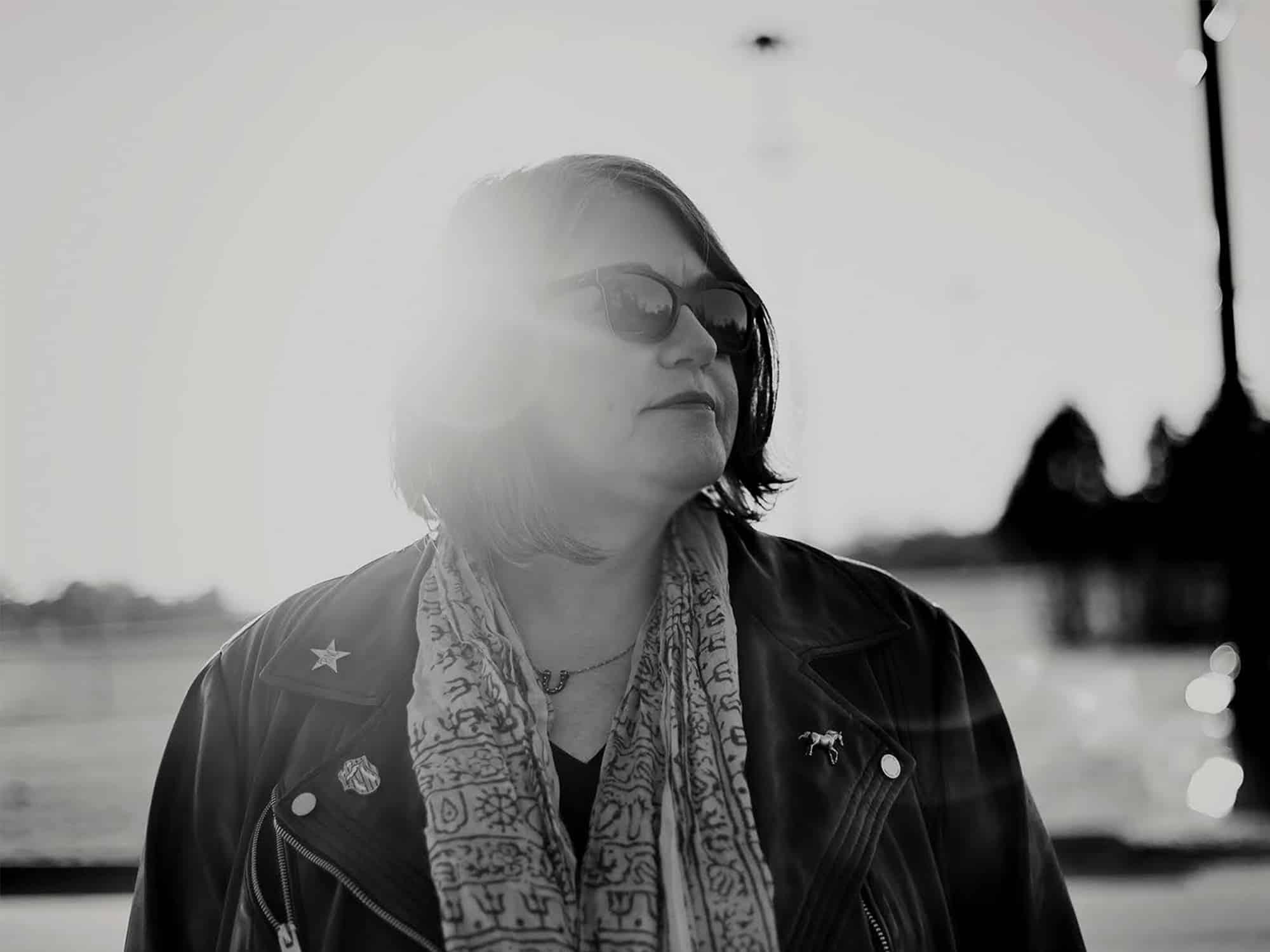 A black-and-white photo shows author Caryn Rose posing outdoors, looking off toward the side of the frame.