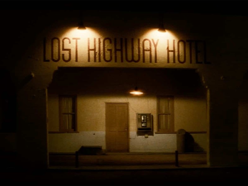 The brightly illuminated façade of a sleazy roadside hotel on the fringes of civilization against a backdrop of impenetrable darkness.