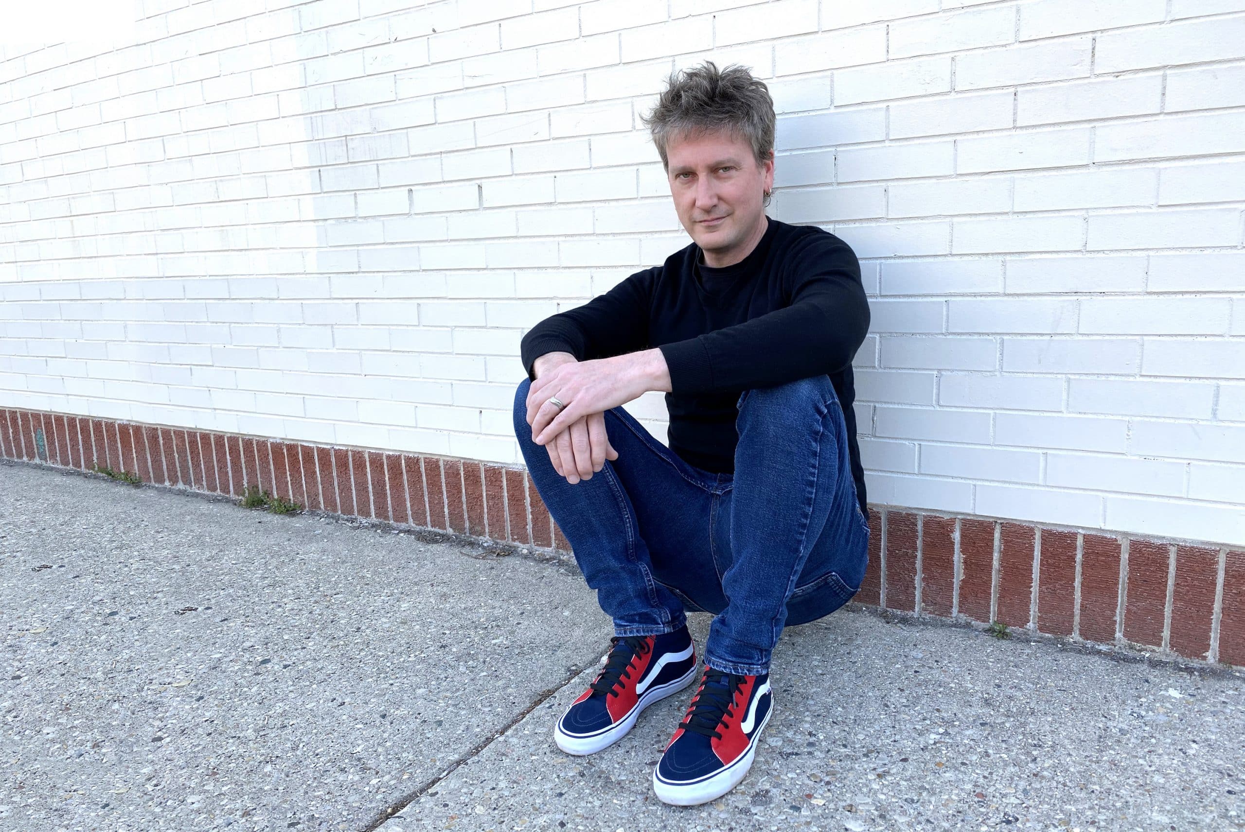 A publicity photo shows Jason Narducy of the project Split Single sitting with his back against a white-tiled wall.