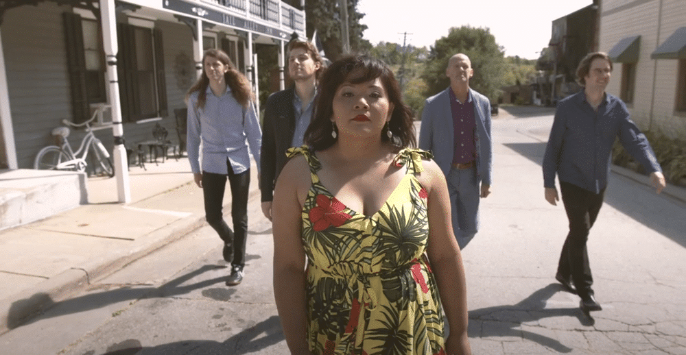 A still from a music video shows musician Leslie Damaso in the foreground, walking down a street followed by the members of Madison band Mr. Chair in the background.