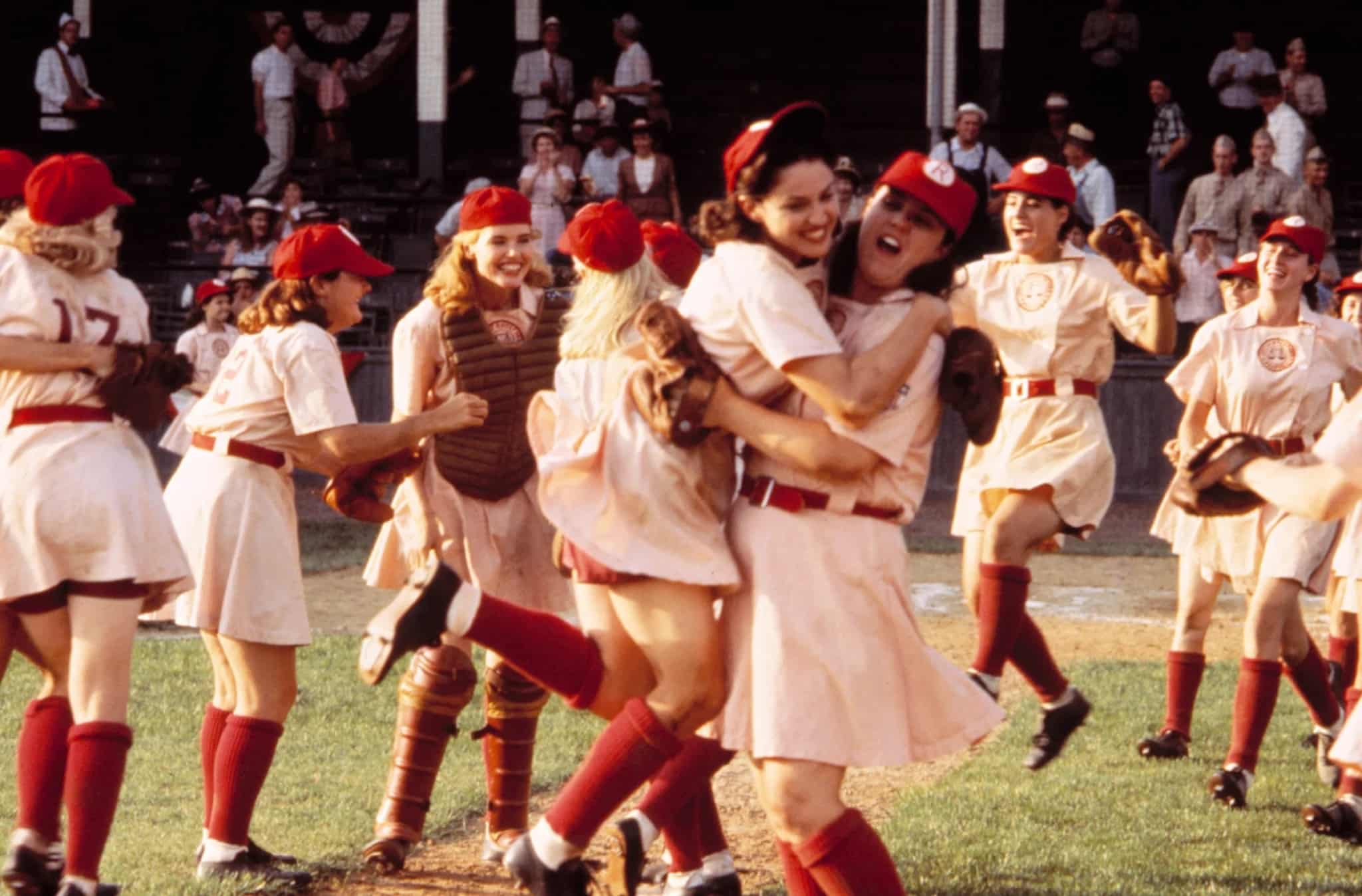 The Rockford Peaches celebrate a nail-biting win on the field. They wear their gloves and other equipment with their pink, short-skirt uniforms and baseball caps. Mae (Madonna) jumps into the arms of her best friend Dorris (Rosie O'Donnell) while Dottie (Geena Davis) laughs and cheers with the rest of the team.