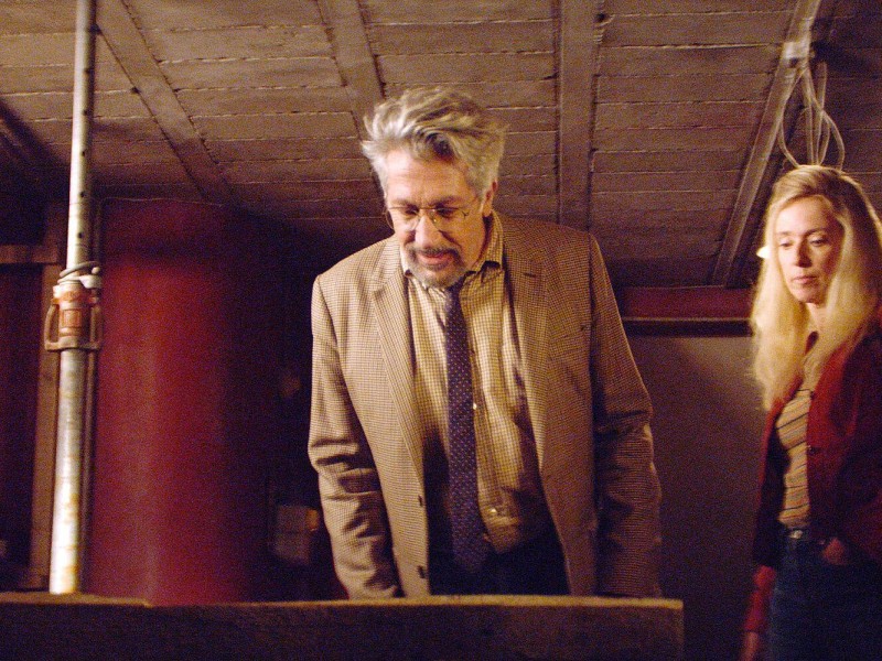 Alain (Alain Chabat) and Marie (Léa Drucker) stand in their basement with red walls, looking down at a hole that contains a mysterious device.
