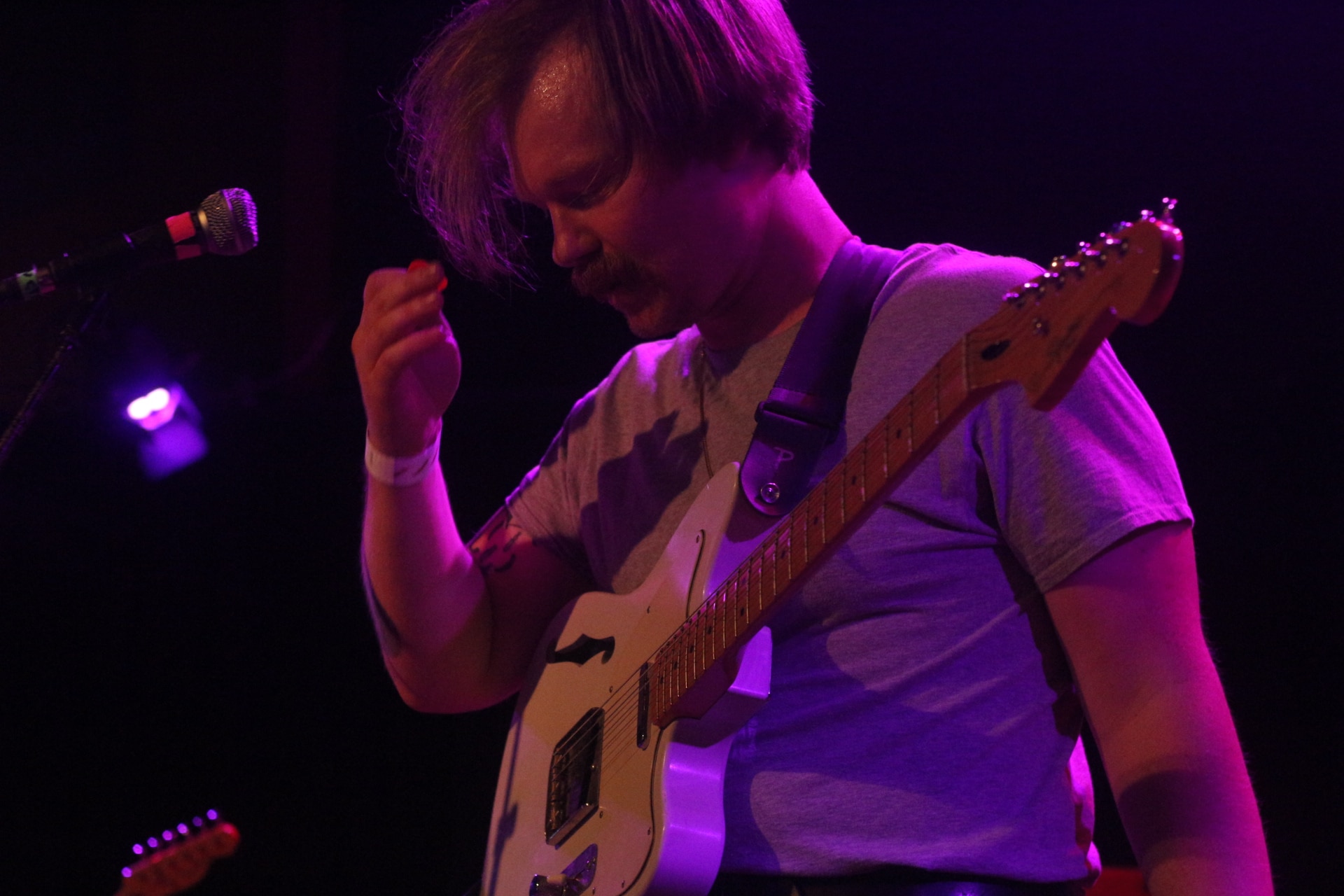 Tyler Fassnacht is shown playing the 2022 Dirtnap Records festival as a member of Proud Parents. He's looking downward, raising his picking hand to his face, wearing a gray t-shirt and playing a white semi-hollow guitar. Photo by Steven Spoerl.
