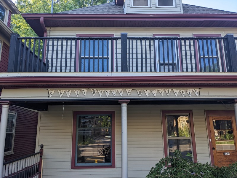 A photo of the now cleaned-up "Halloween house" on East Gorham Street shows the facade of a house with tan siding and maroon-trimmed windows. On the front of the house is a string of pennants that spell out "EVERY DAY IS HALLOWEEN."