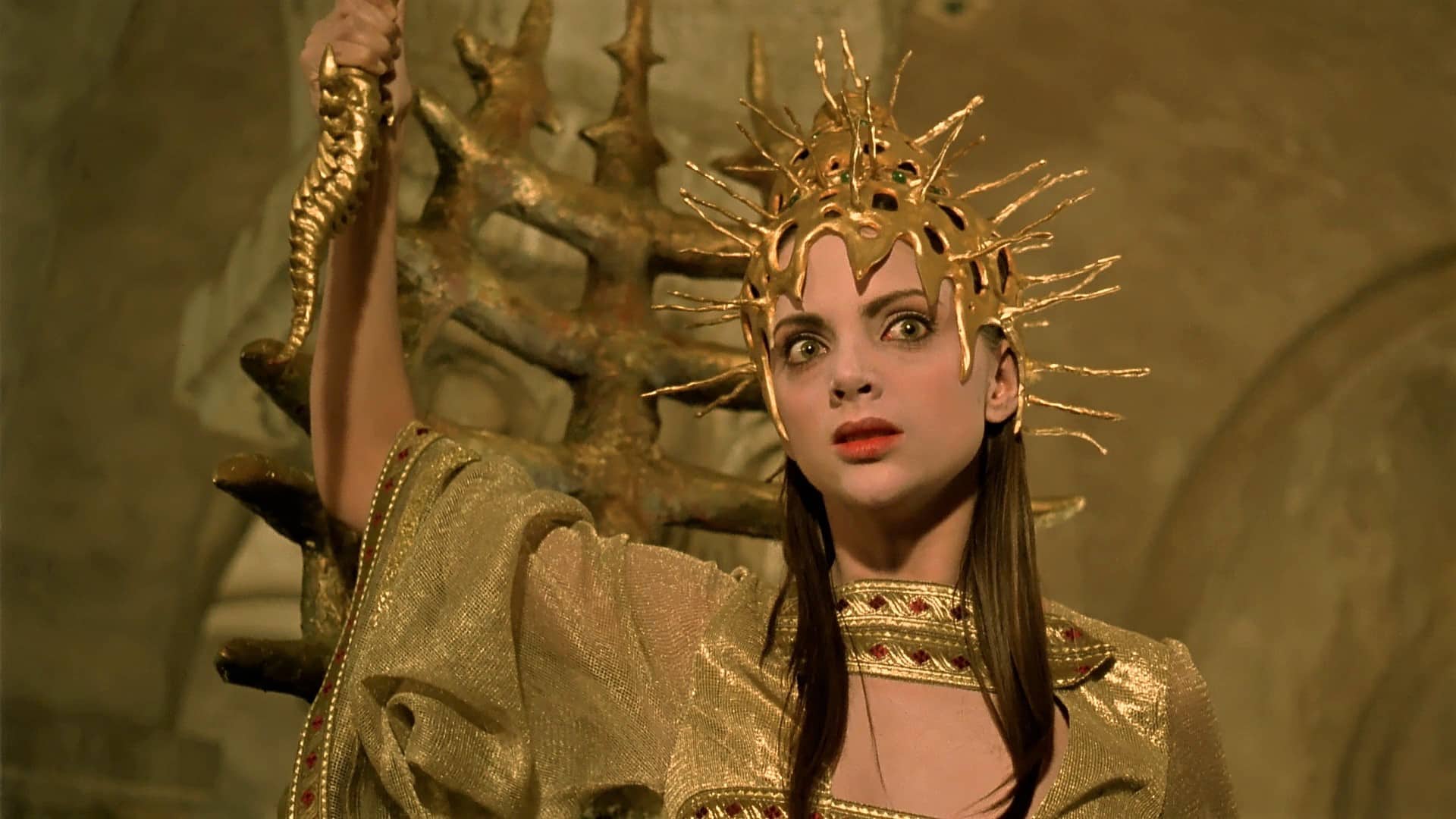 Uxía (Macarena Gómez), dressed in a gold ceremonial outfit, brandishes a gold dagger shaped like a spine.