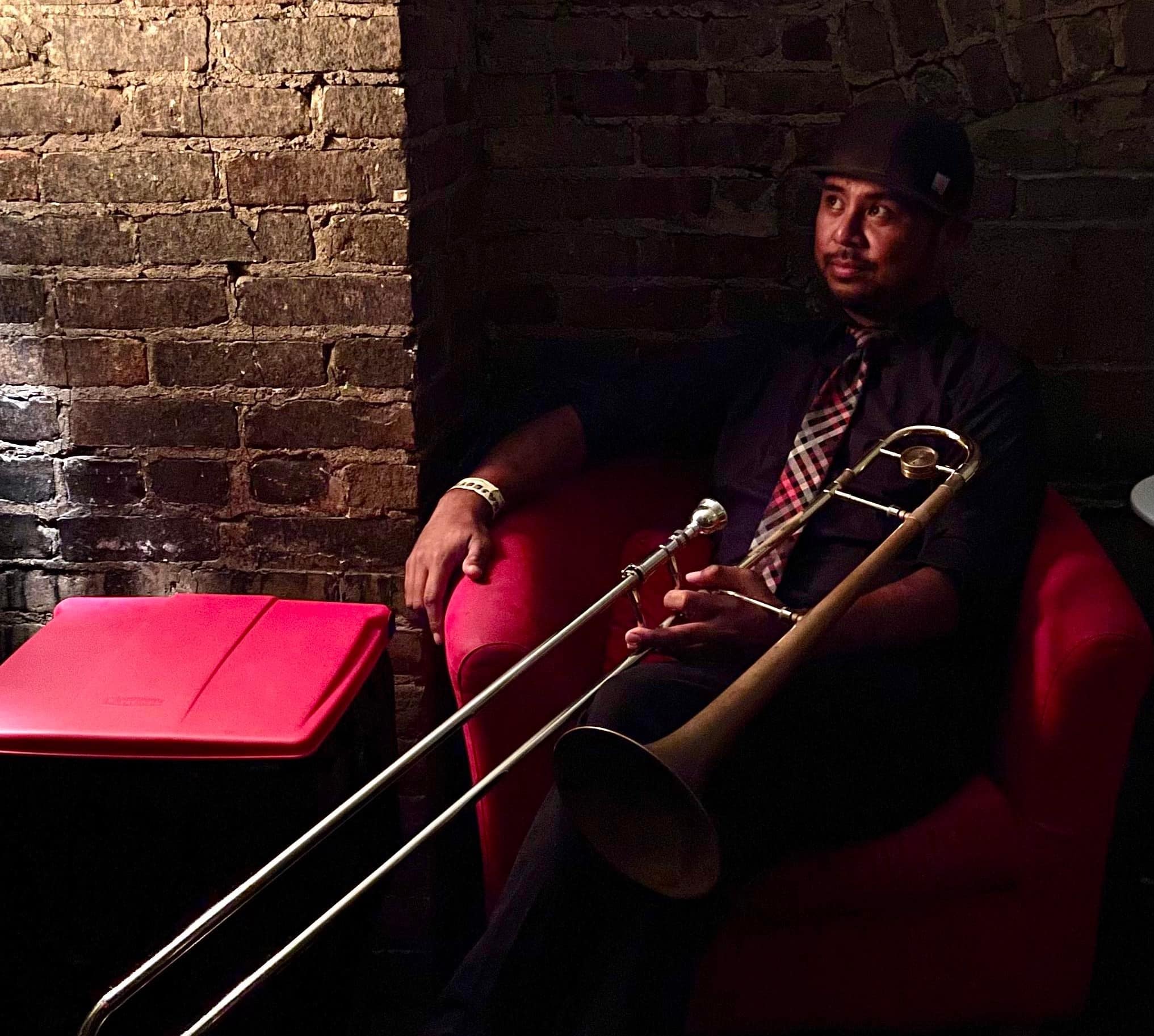 A photo shows musician Darren Sterud seated in a red armchair, holding a trombone over his knee.