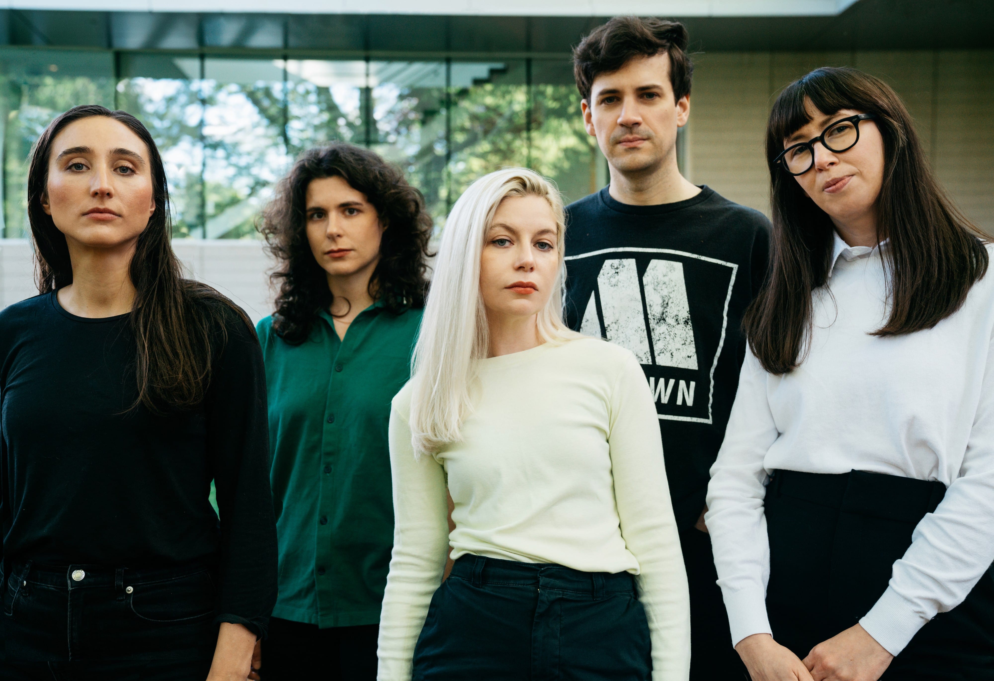 The band Alvvays is shown posing in front of a window out of which trees and greenery are visible.