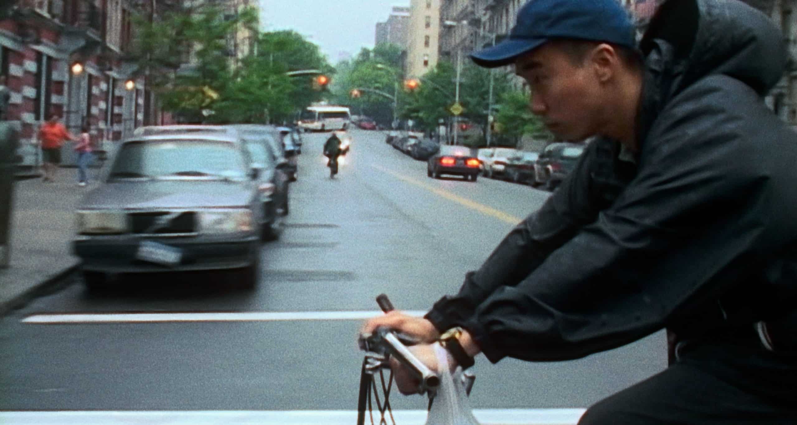Ming Ding (Charles Jang) peddles across a New York City intersection with a Chinese food delivery bag around his left wrist.