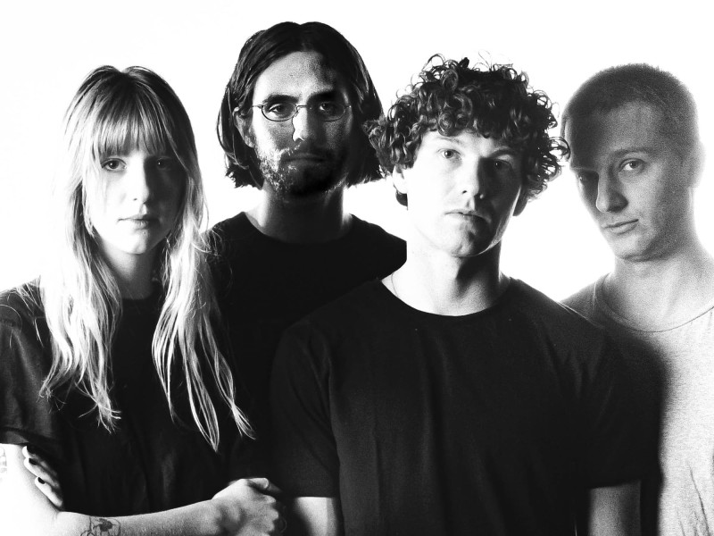 A black-and-white publicity photo of the band Slow Pulp shows the band's four members standing closely together and facing the camera.