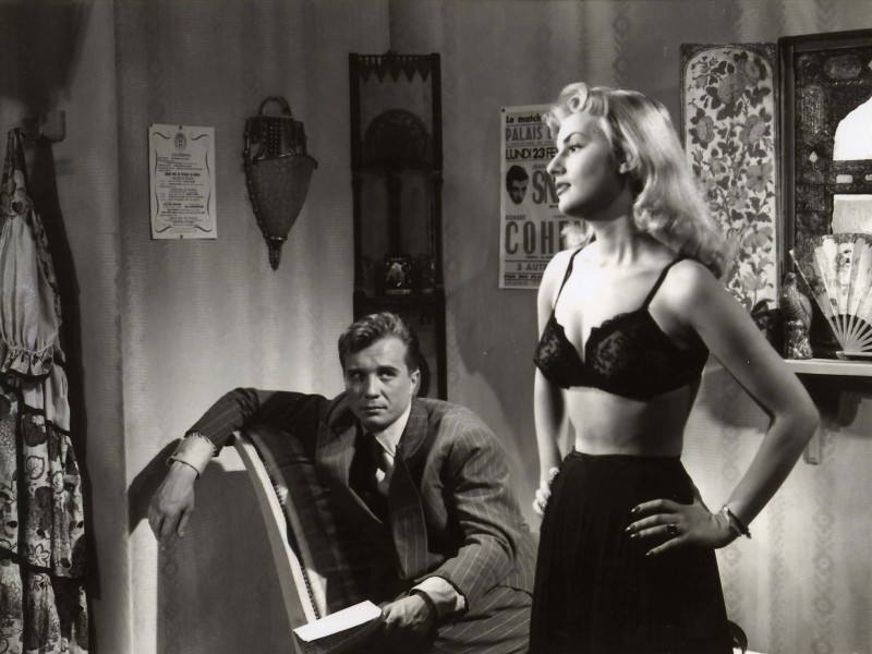 Nightclub dancer Lola (Claude Borelli) stands ready to remove her clothes in front of the rakish Max (Philippe Lemaire), who regards her with smug indifference.