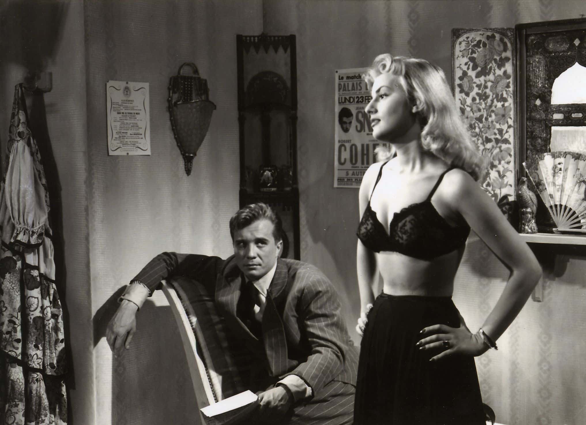 Nightclub dancer Lola (Claude Borelli) stands ready to remove her clothes in front of the rakish Max (Philippe Lemaire), who regards her with smug indifference.