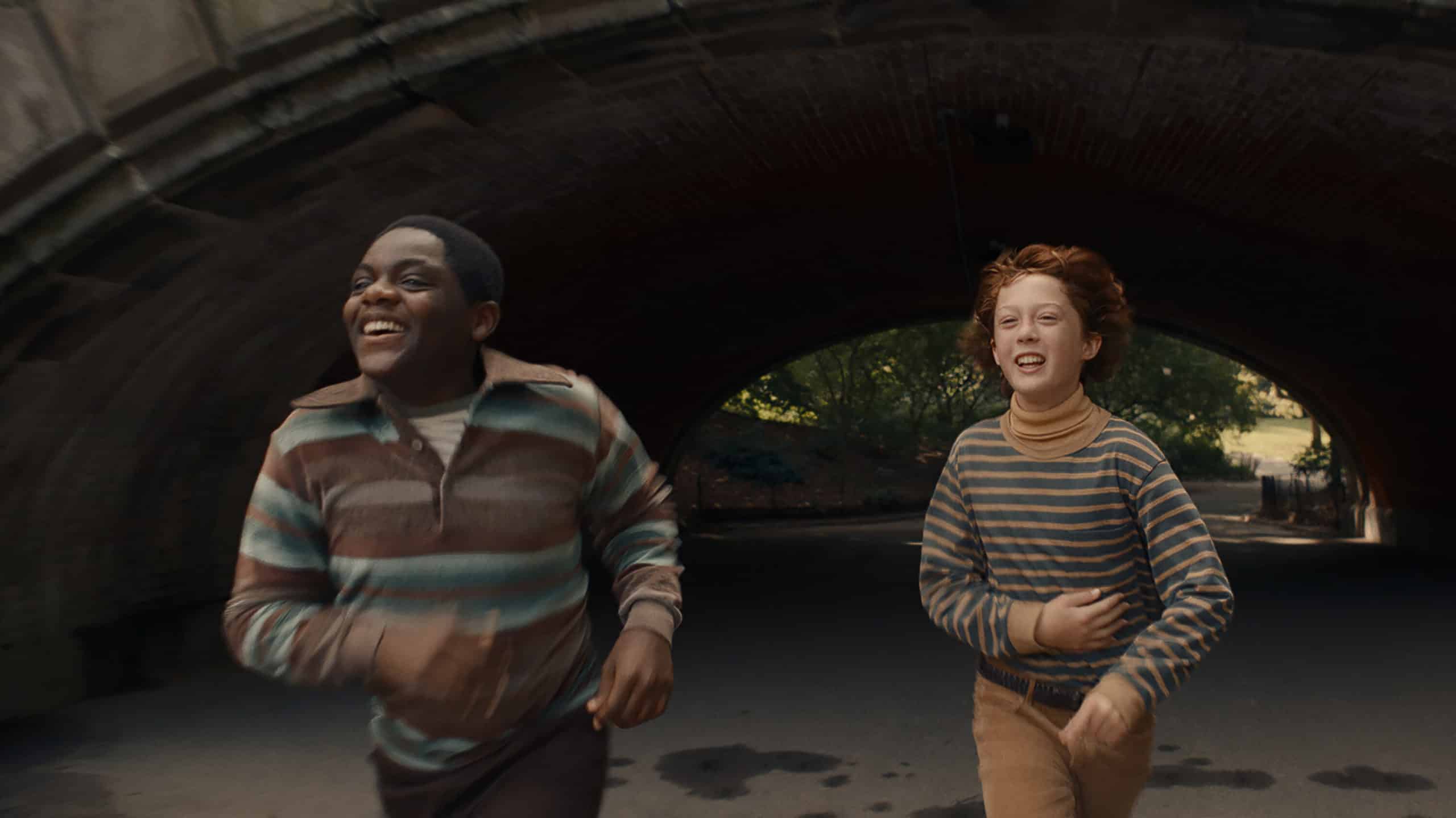 Johnny Davis (Jaylin Webb) and Paul Graff (Banks Repeta) both smile while running through a tunnel under a bridge in a park.
