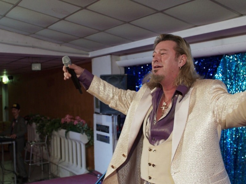 From a glitzy stage, in a glitzy jumpsuit, singer Richie Bravo (Michael Thomas) leads his dozens of fans in a singalong.