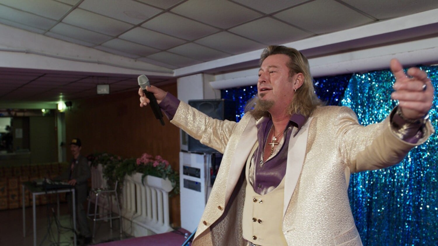 From a glitzy stage, in a glitzy jumpsuit, singer Richie Bravo (Michael Thomas) leads his dozens of fans in a singalong.