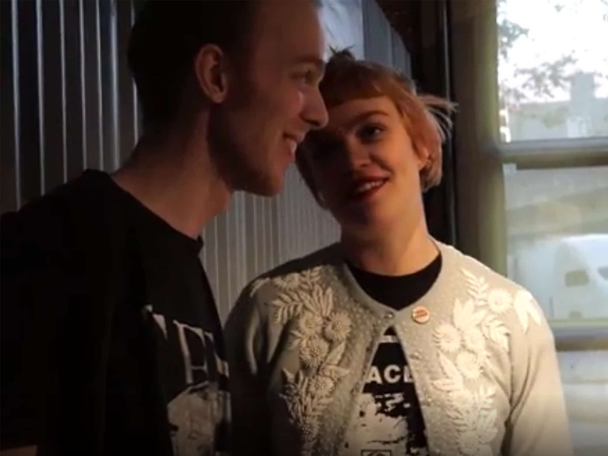 A still from a 2015 video that was produced by "The Guardian" depicting a shared conversation between "Tone Madison" author and musician Steven Spoerl and Perfect Pussy vocalist and journalist Meredith Graves. Both are smiling inside Hand & Detail Car Wash, which played host to a 2015 CMJ showcase that was presented by AdHoc.  