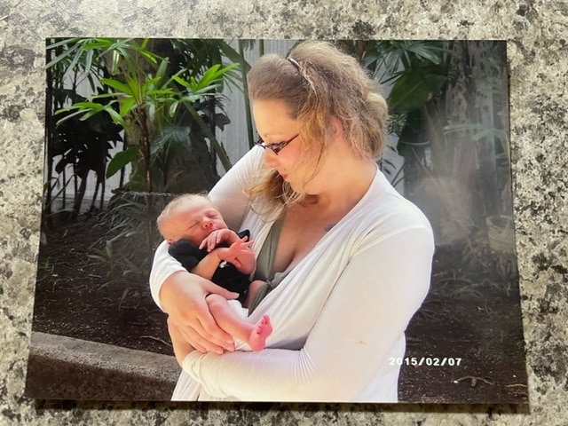 An image of a physical photo on a tabletop shows Tamara Loertscher holding her infant, Harmonious Ellner