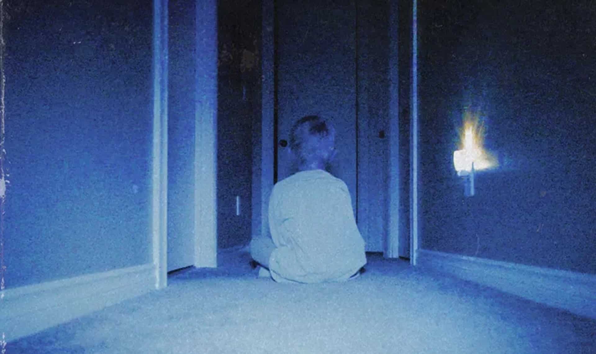 Kevin (Lucas Paul) sits on a carpeted floor facing a door in a darkened hallway. A plug-in nightlight glows to his right.