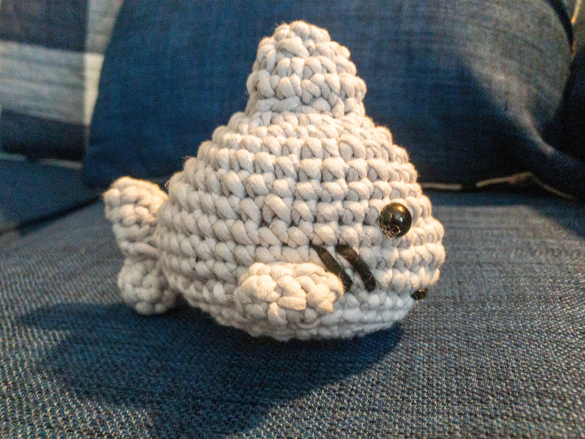A small stuffed shark, crocheted by the author, is shown sitting on a blue sofa cushion.