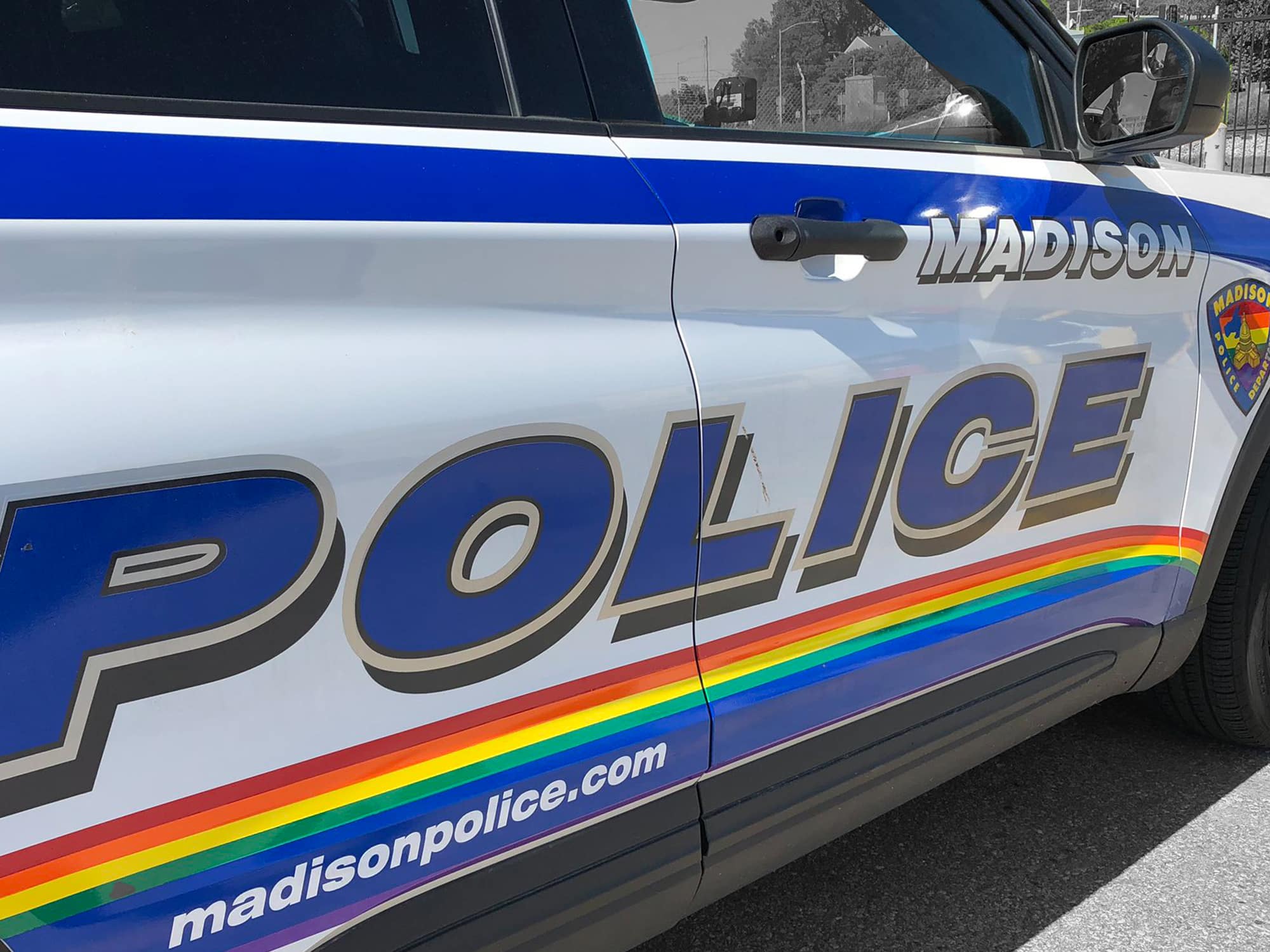 A Madison Police Department car decorated with a special "Pride" wrap, including a rainbow stripe running alongside the side trim of the vehicle and a rainbow-striped version of MPD's logo above the passenger side front wheel well. 