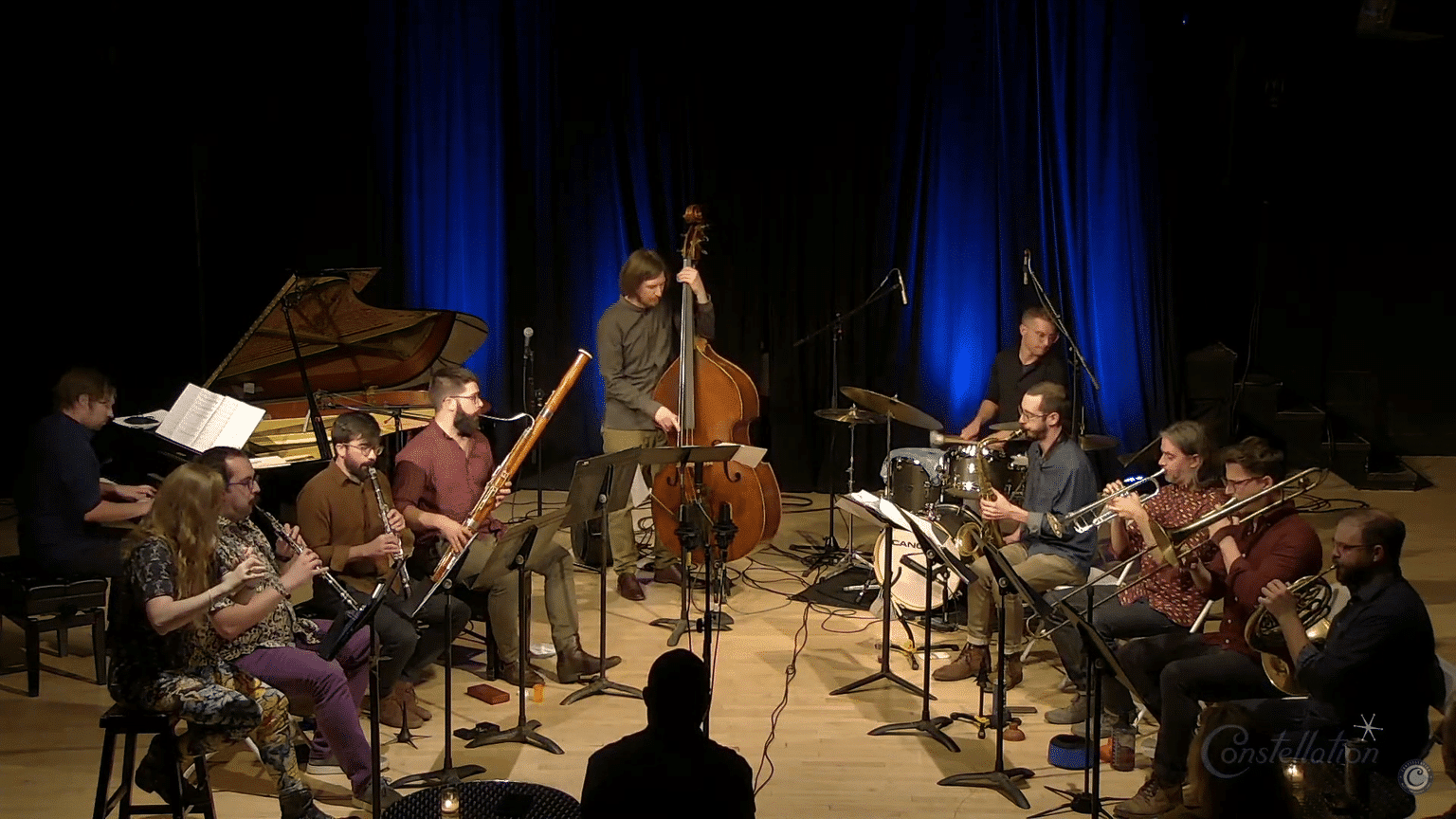 Matt Ulery's Mannerist 11 performs at Constellation Chicago in September 2021 as part of the Ear Taxi Festival. Ulery (center) stands, playing contrabass, with pianist and drummer on either side of him. Woodwinds and brass sit in front (stage right and stage left, respectively).