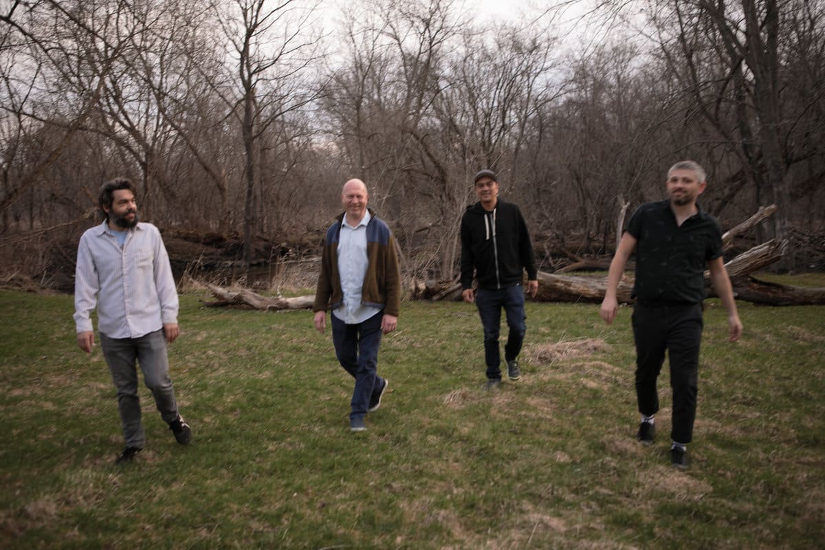 Vacant Church is shown posing in a yard. Tall trees that have lost their leaves can be seen behind them. The photograph is slightly blurry.