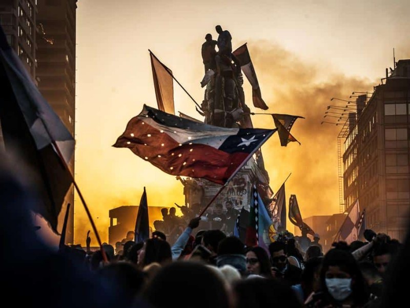Protesters wave a hole-riddled flag of Chile and climb atop a graffiti-covered statue of 19th-century general Manuel Baquedano.