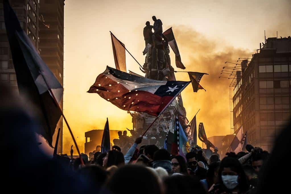 Protesters wave a hole-riddled flag of Chile and climb atop a graffiti-covered statue of 19th-century general Manuel Baquedano.