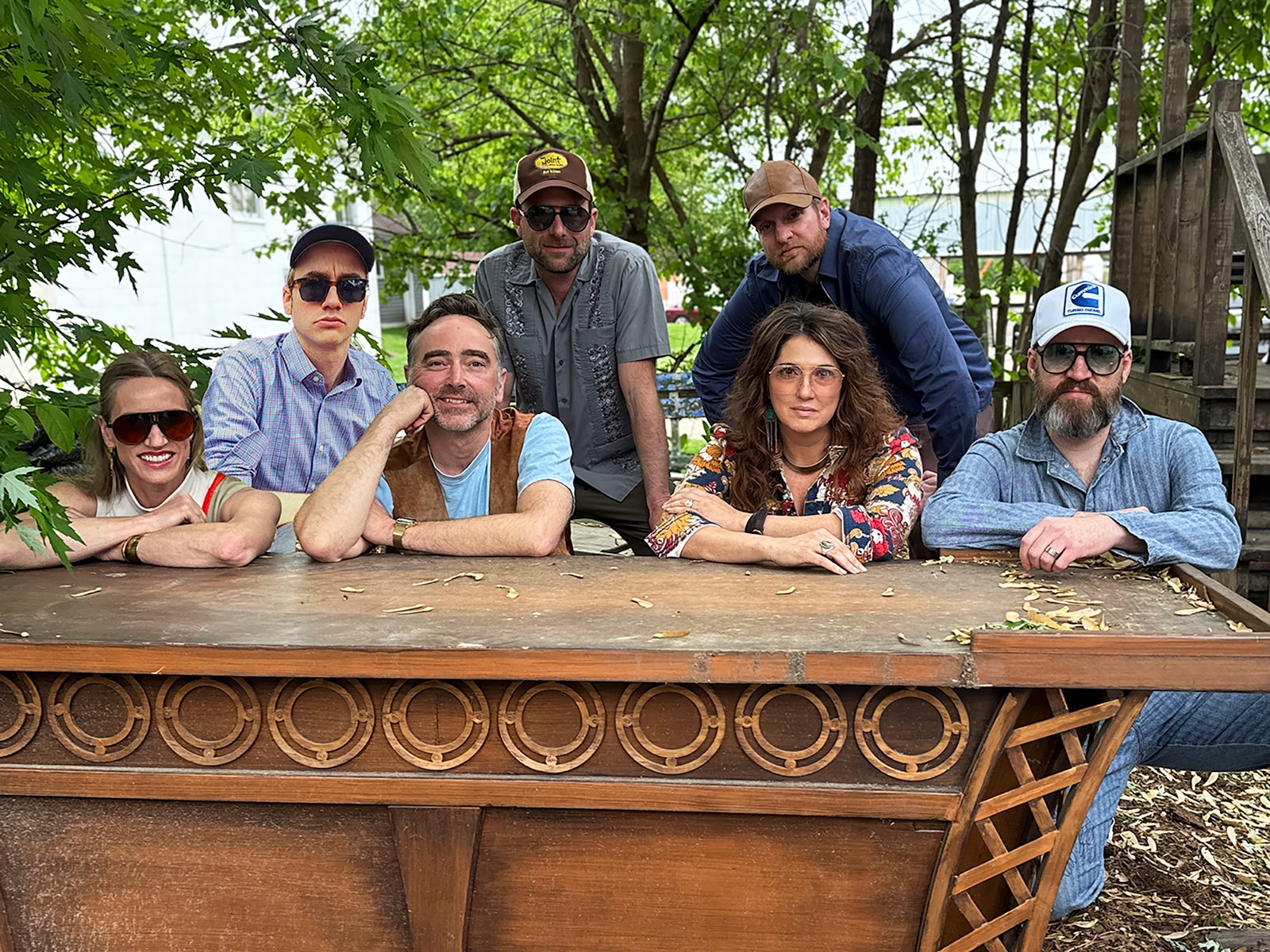 The members of Cribshitter crouch and rest for support on a small wooden table outdoors. Trees are visible in the background.