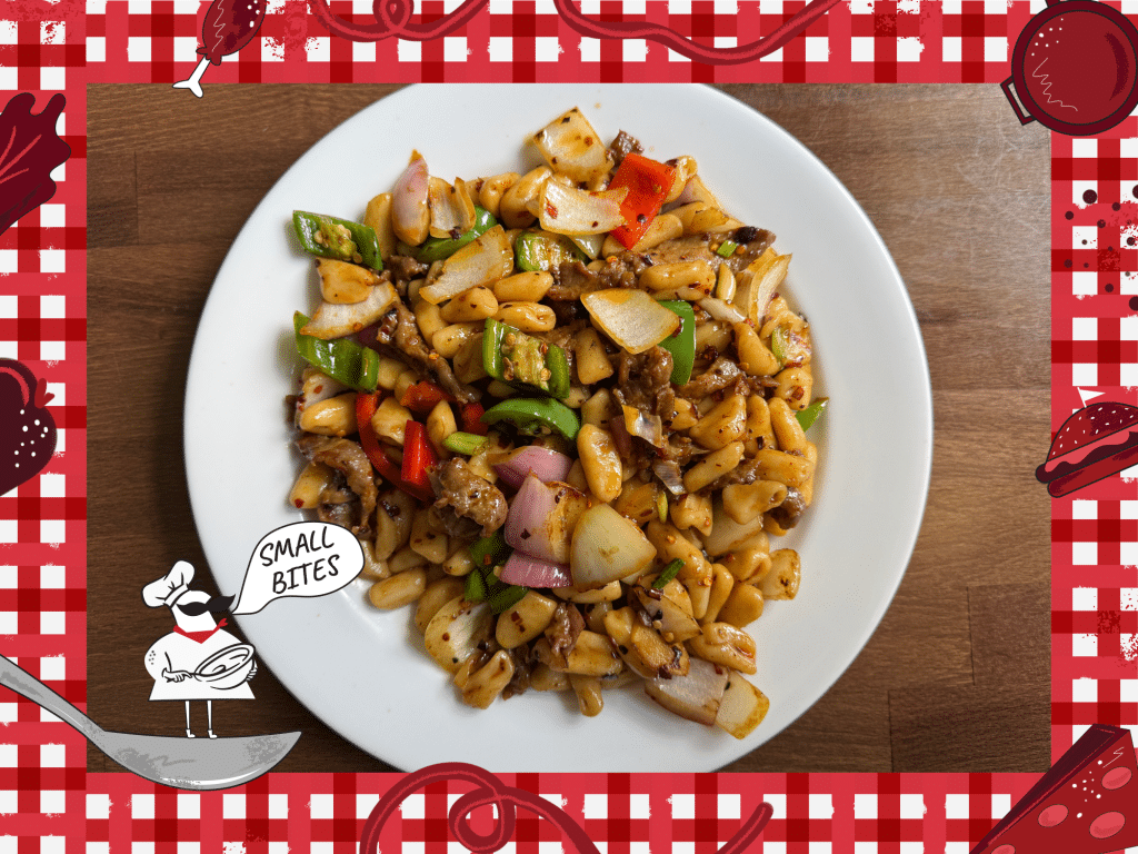 A photo of a white ceramic dinner plate that is filled with freshly prepared cat ear noodles. The dish includes small, flat pasta with chopped onions, chopped peppers, and sauce. Bordering the photo is a red and white checkered tablecloth illustration. In the lower left corner of this illustrated frame is a small chef with an oversized mustache standing on a spoon. The chef's speech bubble reads "Small Bites."