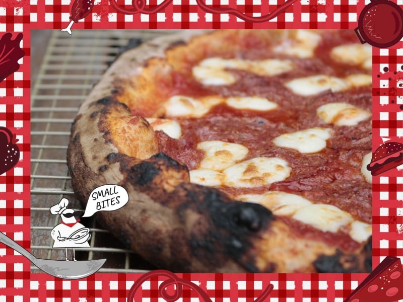 A close-up photo of half of a handmade pizza fresh out of the oven. It is sitting on a metal cooling rack. The crust is slightly burnt. Bordering the photo is a red and white checkered tablecloth illustration. In the lower left corner of this illustrated frame is a small chef with an oversized mustache standing on a spoon. The chef's speech bubble reads "Small Bites."