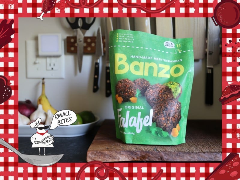 Photo of a bag of frozen falafel locally prepared by Banzo, a pantry staple for the author's disabled household. The green bag with yellow and white text reading "Hand-made Mediterranean Banzo Original Falafel" sits upright on a kitchen counter cutting board in front of some knives mounted on a rack. Bordering this photo is a red and white checkered tablecloth illustration. In the lower left corner of this illustrated frame is a small chef with an oversized mustache standing on a spoon. The chef's speech bubble reads "Small Bites."