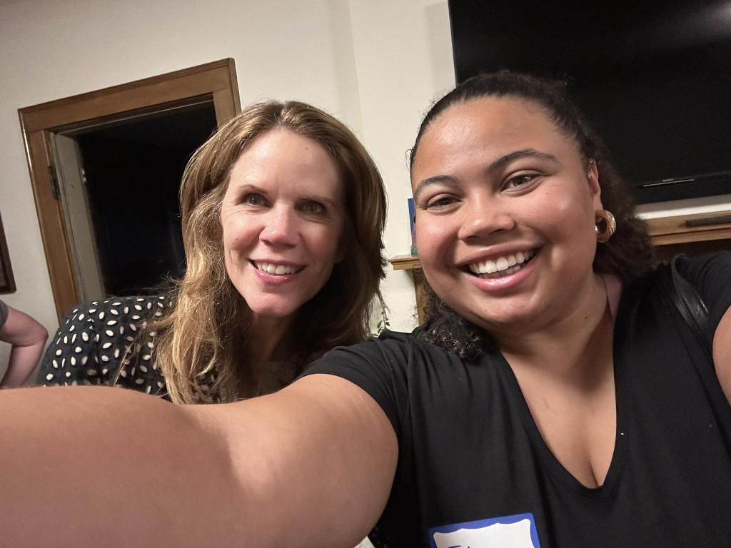 In a living-room area, Juliana Bennett, on the right, takes a selfie with Wisconsin Supreme Court candidate Chris Taylor. Both smile widely and stare directly at the camera lens.