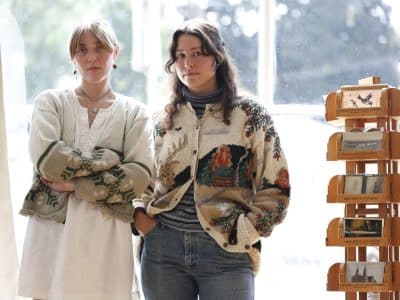The Spine Stealers' Kate Ruland (left) and Emma O'Shea (right) are shown in their Madison studio, standing next to a carefully-curated postcard collection that's housed in a wood stand.