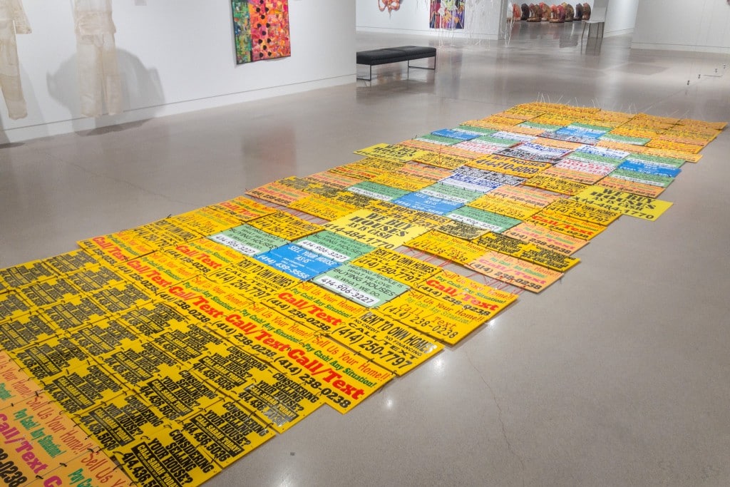 Bright yellow 130 "Cash for Homes" signs lay on the floor of an art gallery, linked with zip ties.
