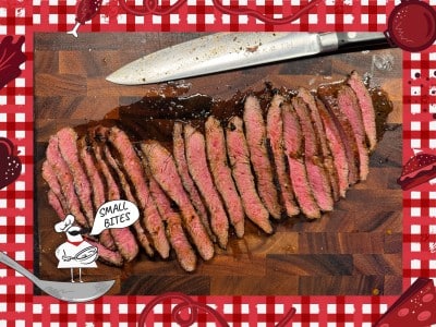Photo of slenderly sliced pieces of medium-done steak sitting on a wooden cutting board. A kitchen knife sits on the board behind the steak with the blade facing away from the camera. Bordering this photo is a red and white checkered tablecloth illustration. In the lower left corner of this illustrated frame is a small chef with an oversized mustache standing on a spoon. The chef's speech bubble reads "Small Bites."