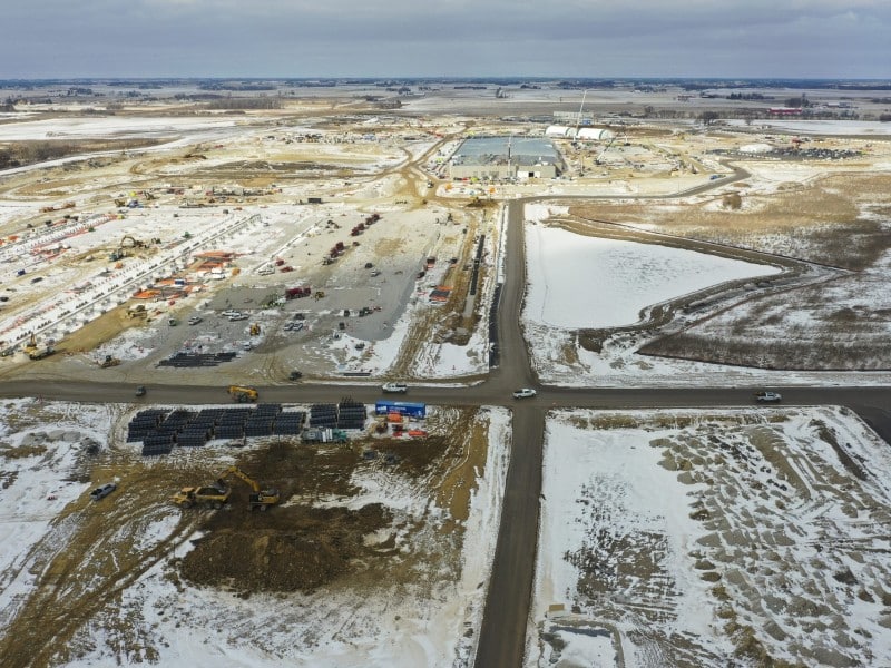 Distant aerial photo of a rural landscape covered in patches of snow. A large construction site is in operation in parts from the foreground into the background with various machines and equipment.