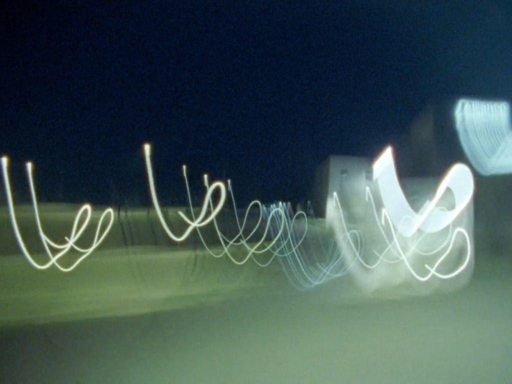 Blurry still frame taken from the experimental documentary "The Phalanx" shows a series of fluorescent light trails over footage that is zooming through part of the town of Ripon, Wisconsin, at night.